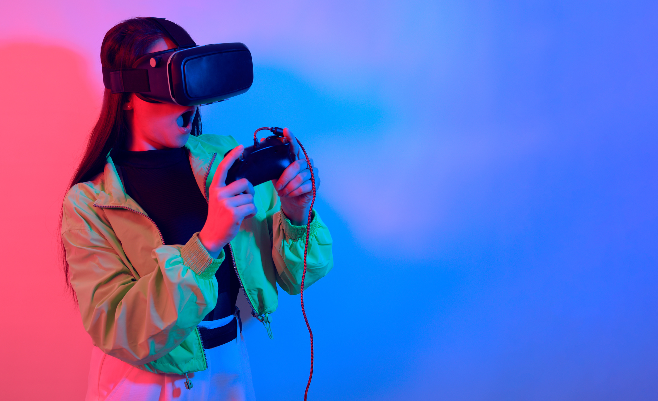 A shocked girl in neon with VR glasses holds a gamepad in her hands and plays games. Virtual world, technology.